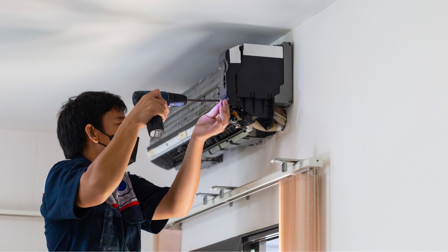 A man uses a screwdriver to adjust a component of an AC unit.