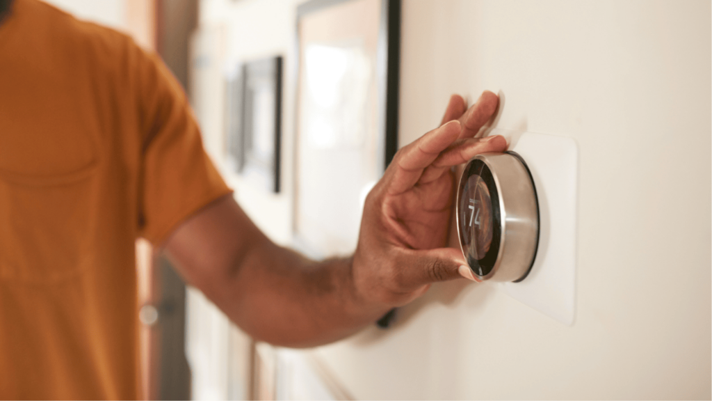 A man adjusts a modern circular shaped thermostat in his home.