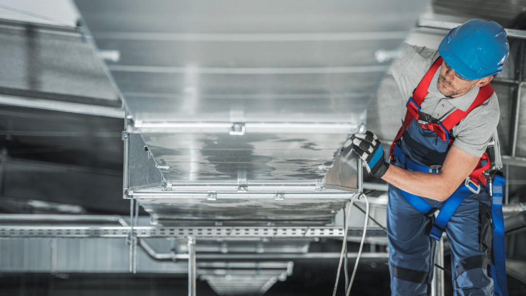 An HVAC technician works on the ducts of a commercial heating system.